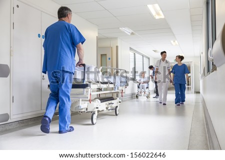Male nurse pushing stretcher gurney bed in hospital corridor with doctors & senior female patient Royalty-Free Stock Photo #156022646