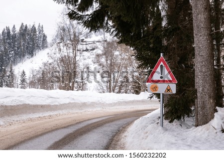 Red triangle road traffic warning sign - Other Danger. Crossroads with cross-country skis paths . Snow covered road, trees and mountains. Ski resort Schladming Dachstein, Austria.