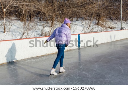 Lovely young woman riding ice skates on the ice rink. Girl skating on ice in a winter frosty day