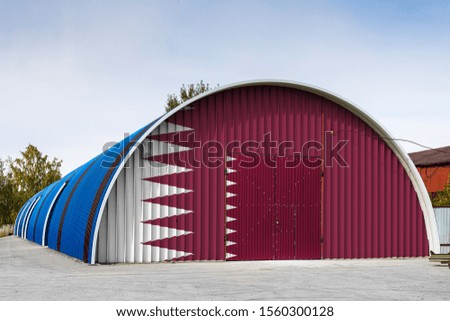 Close-up of the national flag of Qatar
 painted on the metal wall of a large warehouse the closed territory against blue sky. The concept of storage of goods, entry to a closed area, logistics
