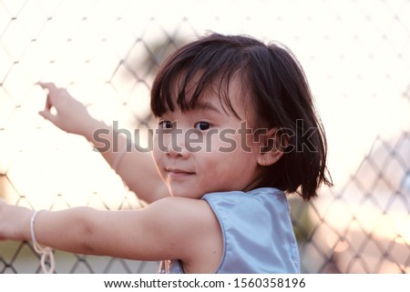 Cute Asian child girl is smiling happily while standing by the fence. Selective focus