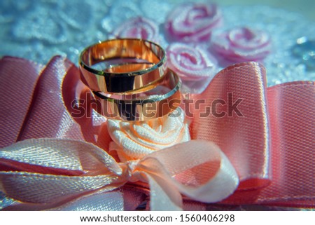 Classic wedding rings, selective focus, close-up. Gold rings of the bride and groom shine and shimmer against the pink ribbons and flowers from textiles.