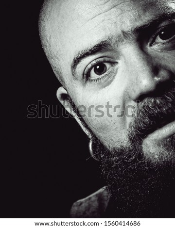 Black background studio shot of a long-bearded, balding hispster man sniffing with amazement or frightened.
