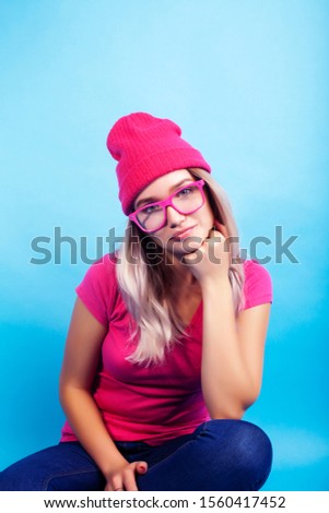 young pretty teenage modern hipster girl posing emotional happy on blue background, lifestyle people concept