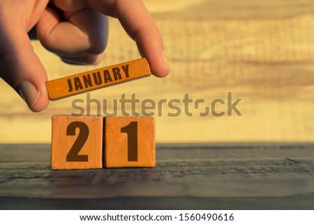 january 21st. Day 20 of month, calendar on a wooden cube. a woman's hand puts the name of the month on the number of the month on a wooden background winter, day of the year concept.