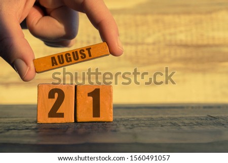 august 21st. Day 20 of month, calendar on a wooden cube. a woman's hand puts the name of the month on the number of the month on a wooden background summer, day of the year concept.