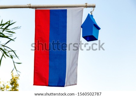 Real Flag of Russia or Russian Federation on a flag pole hanging near a tropical oleander flowers and sunny trees.