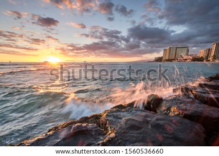 Sunset at Waikiki Beach, Hawaii with waves crashing again rocks