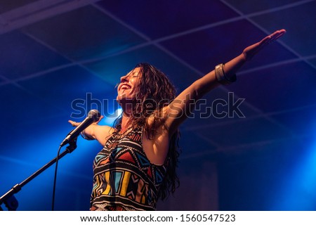 a female musician is viewed from a low angle as she sings and smiling with the audience with her hands raised up during a performance 