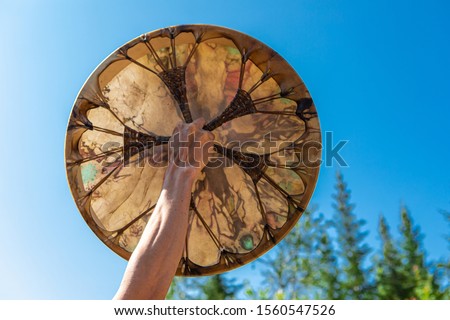 man holding his sacred drum in the clear sky, close up on hand holding native American drum isolated in blue sky and trees background