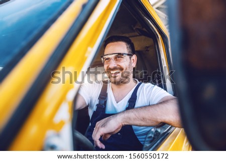 Smiling handsome unshaven worker driving vehicle on construction site.