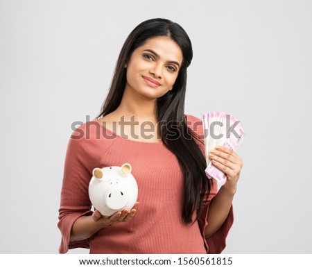 Pretty Indian young woman saving money in piggy bank