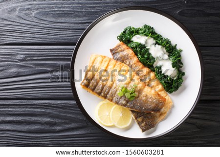 Serving fried sea bass fillet with spinach and lemon closeup on a plate on the table. horizontal top view from above
 Royalty-Free Stock Photo #1560603281