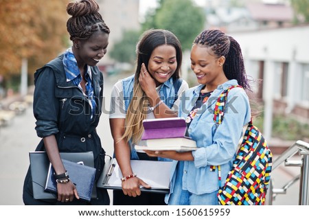 Three african students female posed with backpacks and school items on yard of university and look at tablet.