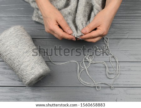 Female hands knitting closeup. Gray woolen linen and a bobbin of yarn on a gray wooden background. View from above. handmade.