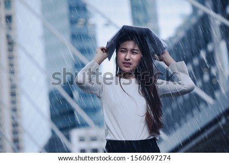 Girl in the heavy rain storm cover head with newspaper for economic obstacle passing concept. Royalty-Free Stock Photo #1560697274