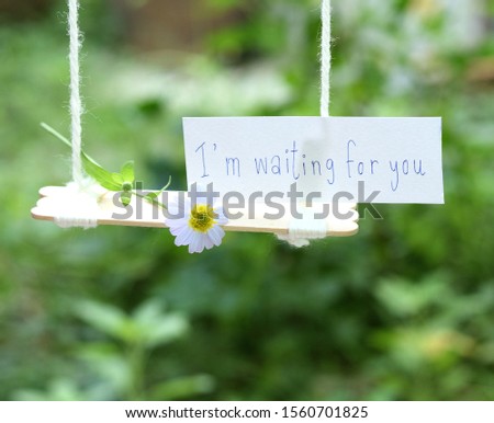 a white flower lying  on a swing with words " I'm waiting for you " written by hand on a piece of white paper 
