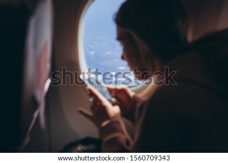 girl who flies for the first time and sits on a chair by the window enjoys the view from the window, takes pictures, focus on window view, noise effect