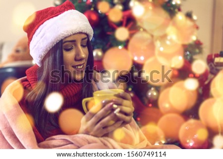 young woman in Santa hat drinking tea or coffee over christmas tree background at home