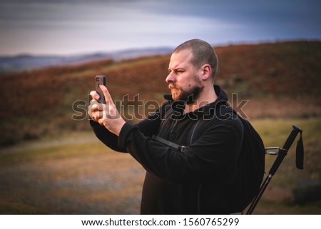 A man taking a photo on a smart phone of a view in the Lake District