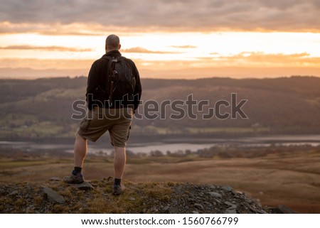 A man in hiking clothing looking at Coniston water from a mountain peak