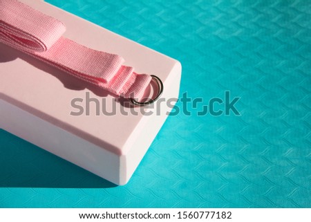 Yog set of accessories for yoga. A pink cube and a strap for stretching lie on a blue rubber rug.