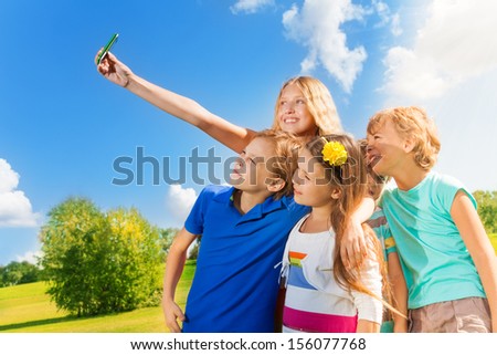 Beautiful blond girl taking picture of friends standing together in the park on sunny day