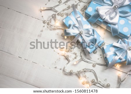 Top view of blue gift boxes with white and blue ribbon and lights decorated with pearls on white wooden background with copy space. Vintage toned photo. Christmas and New Year concept.