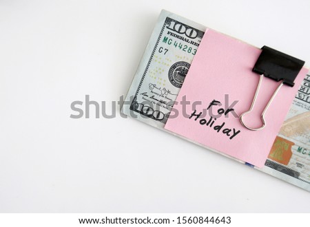 Cash money dollars banknote clip with pink note with text written FOR HOLIDAY on white copy space background - concept of budget planning and savings for coming holiday season