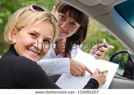 Proud successful woman purchasing a car turning to smile at the camera as she and the saleslady prepare to sign the documentation and finalise the deal