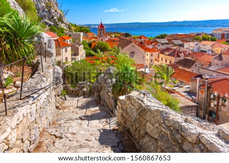 Sunny red roofs, Old city street with stone stairs and Church of St Michael in town and port Omis, popular tourist spot in Croatia Royalty-Free Stock Photo #1560867653