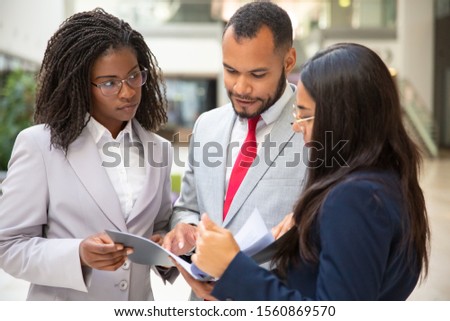 Focused business team reading agreement together. Business man and women standing in office hall and holding open folder with document. Expertise concept