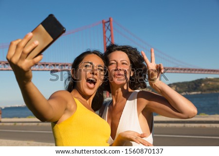 Happy friends taking selfie with smartphone. Cheerful multiethnic women standing near river and taking selfie via mobile phone. Technology concept