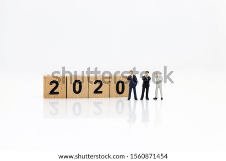 Miniature people: Businessman standing with stack of coins and wooden block 2020. Image use for investment for benefit of year, business concept.