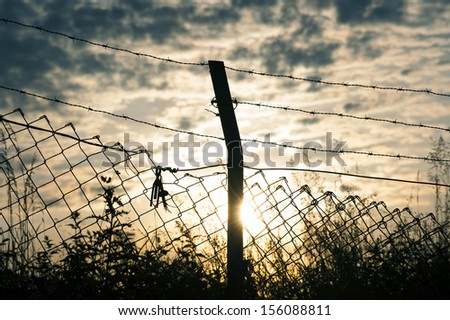Close-up on a pole with barbed wire, sunset in background