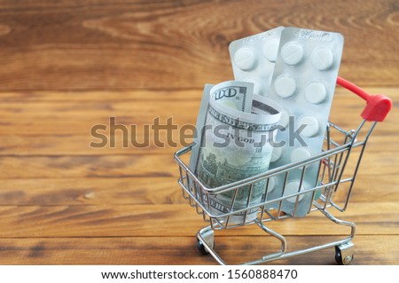 Shopping cart with tablet blisters and dollar banknote. Spending money on pills and expensiveness of medicine concept.