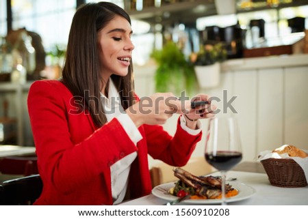 Attractive businesswoman in suit sitting in restaurant and taking picture of food over smart phone.