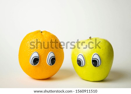 Orange and green apple with eyes. Orange and apple are looking at each other. Funny cute picture of fruits. The concept of friendship, sympathy, love. Light background, place for text.