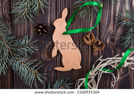 Handmade Christmas wooden rabbit on brown background decorated with cones, nutshells and fir branches