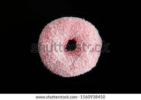 Pink donut. One donut with with white coconut topping, isolated on black background. Top view.