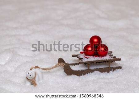 Christmas greeting card template. A little polar bear pulls a sleigh with three red Christmas balls through the snow. Copy space for your design. Macro photograph.