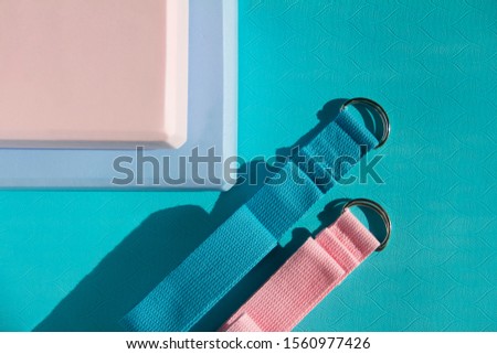 Set of yoga accessories. Pink and blue cube and straps for stretching are on a light blue rubber mat.