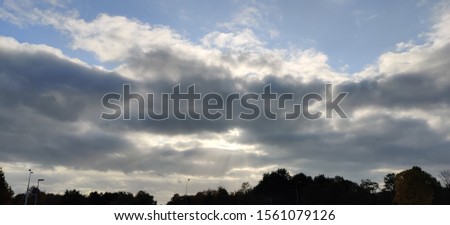 Cloudy sky with sun peeping through on tree silhouette