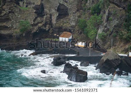 Capelas is a village near a beautiful bay on the southern coast of São Miguel Island, Azores, Portugal. Pictured is a very small harbor area with structures. Waves crashing on the black lava shore.