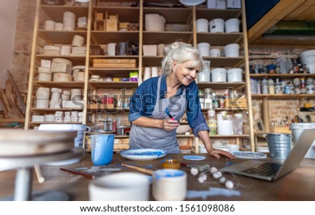 Mature woman pottery artist using laptop in art studio 
