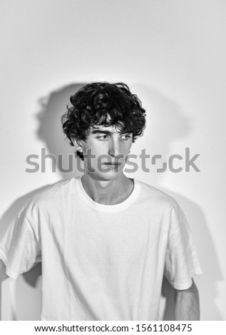black and white photography. portrait of young handsome Italian model boy with dark curly hair posing for a fashion shooting on white background