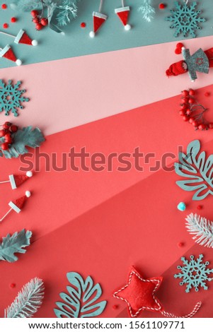 Christmas flat lay with frame from decorations - winter leaves, dolls, garland and snowflakes. Above view of multicolored geometric layered paper background in red, orange, pink, magenta and silver.