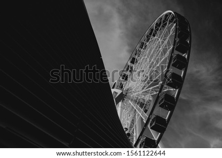A grayscale low angle shot of a Ferris wheel under the cloudy sky