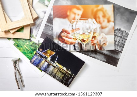Canvas prints, colorful photos of St. Petersburg and drinking people, tool for wrapping. Photographs, stretcher bars and canvas pliers on white wooden table. Photos printed on glossy synthetic canvas