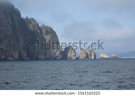 Beautiful rock formations in the bay with green grass and water as well as clouds and blue skies in Alaska